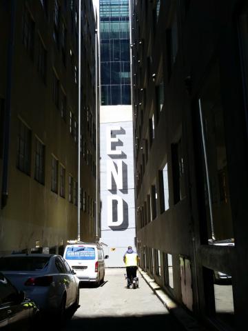 A dark laneway ending at a sunlit wall adorned with street art consisting of the word "END" in bold capital letters.